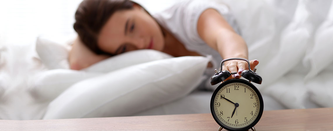Vrouw slapend in bed die reikt naar haar alarmklok
