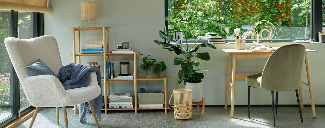 Off-white teddy fauteuil bij het raam en een roomdivider van bamboe, bamboe lantaarn op de grond naast een bamboe bureau en een olijfgroene eetkamerstoel