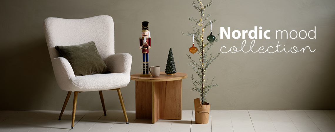 Stoel met kussen, salontafel met kerstfiguurtje en een smalle kerstboom versierd met glazen kerstballen