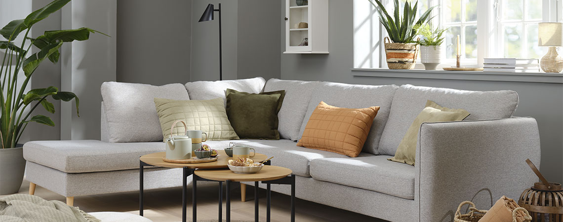 Inrichting van de woonkamer met grijze sofa en oranje, groene en beige kussens