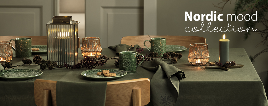 Tafel gedekt met groene kerstborden, groene kerstmokken, lantaarns en theelichthouders en kaarsen 