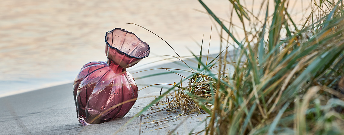 Decoratieve glazen vaas in auberginekleurig glas op het strand 