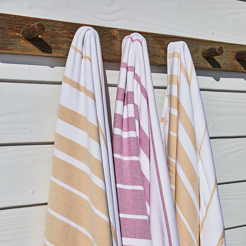 Serviettes de plage rayées en blanc, orange et rose fuchsia suspendues à un mur en bois