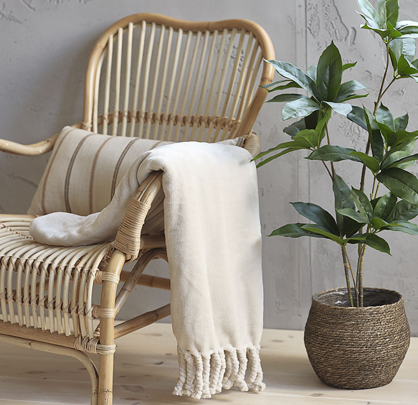 Plaid beige sur chaise longue en rotin et plante artificielle en cache-pot