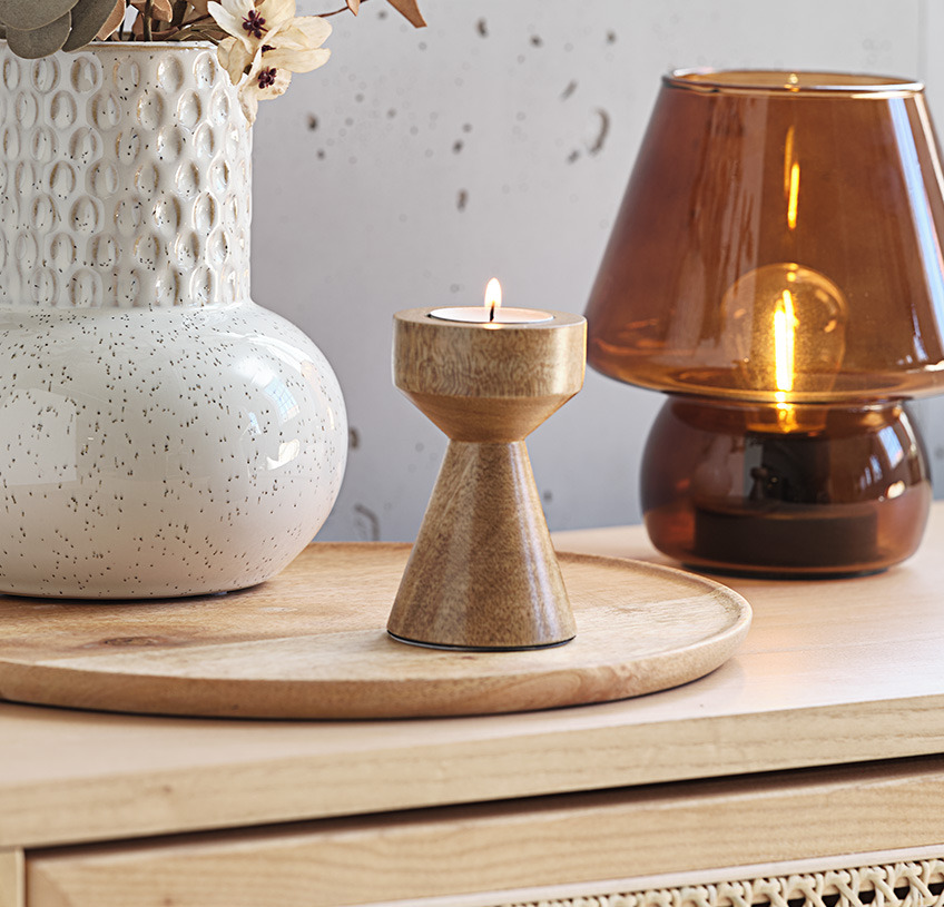 Photophore en bois de manguier, vase blanc et lampe en verre brun sur un dressoir en bois