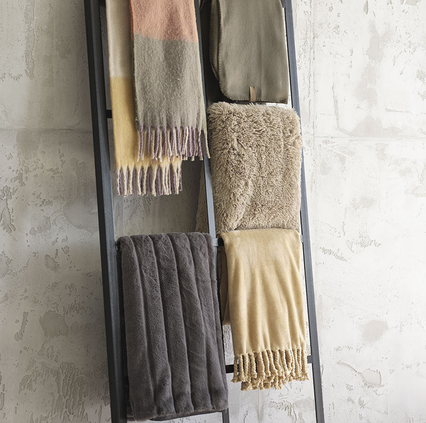 TUSENFRYD plaid in geblokte kleuren, DAGLILJE groene fleeceplaid, MYRFIOL plaid uit imitatiebont, STAVKLOKKE donkergrijze plaid en BONDEROSE fleeceplaid met franjes Fleeceplaids op een decoratieve ladder