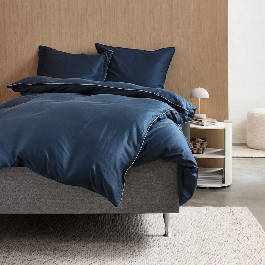 Satijnen dekbedovertrekset in donkerblauw met helderblauwe rand op bed in slaapkamer