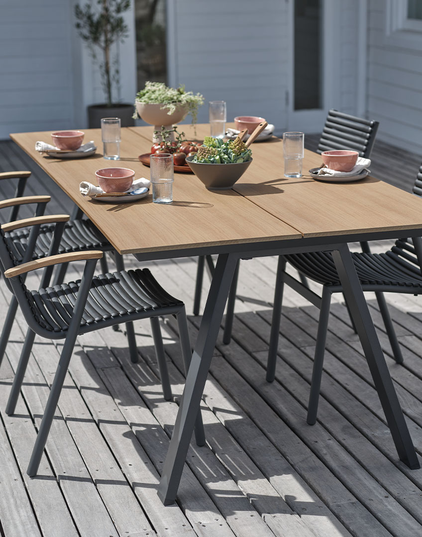 Buitentafel met tafelblad van kunsthout en stapelbare kunststof stoelen met armleuningen van gerecycled teakhout 