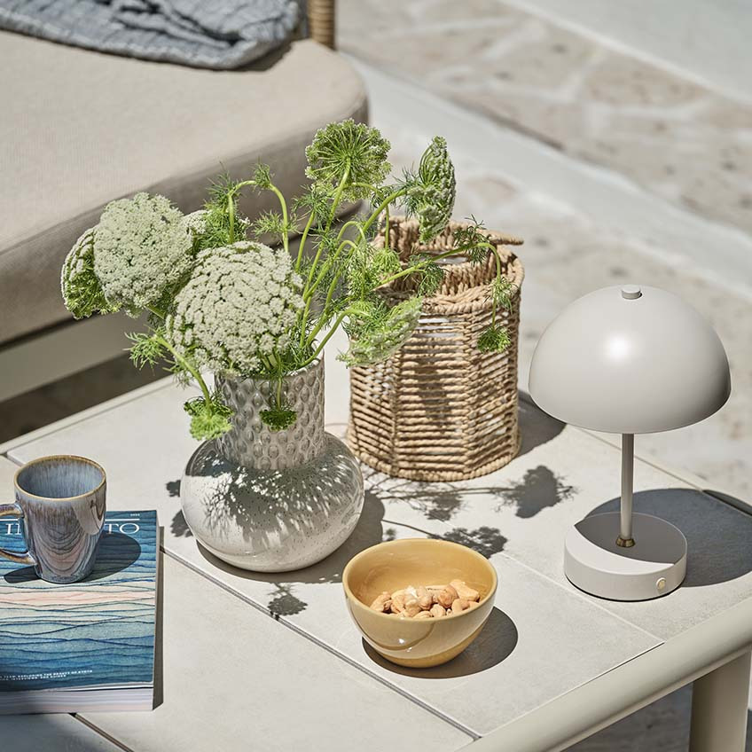 Petite table de jardin avec diverses décorations, dont une lampe à piles, un vase et une lanterne