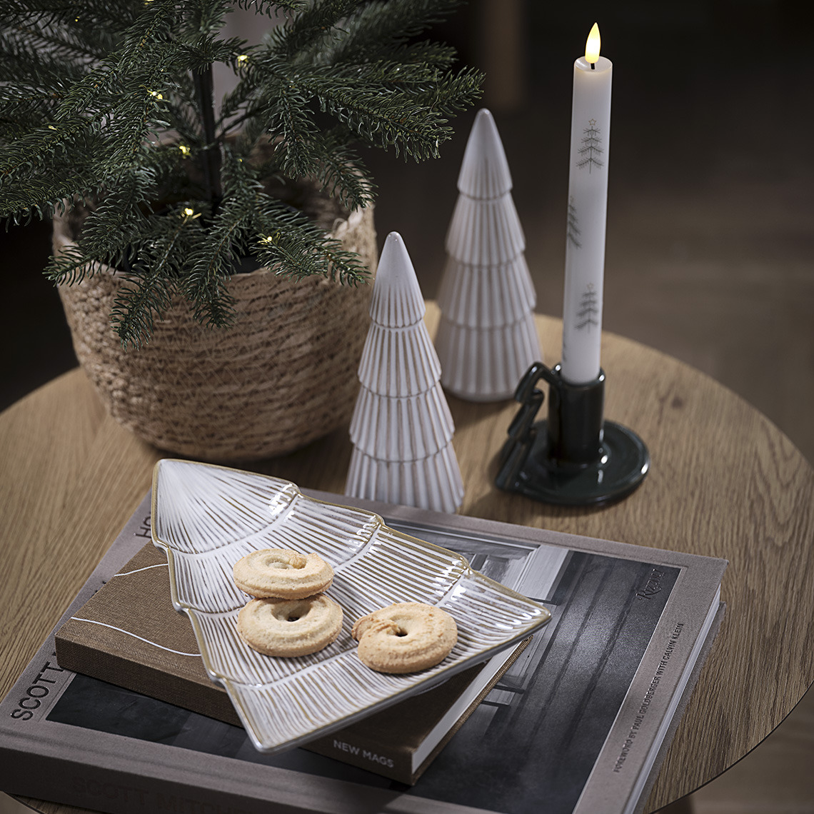 Decoratieve schaal met koekjes, twee decoratiebomen en kandelaar met kaars op een tafel 