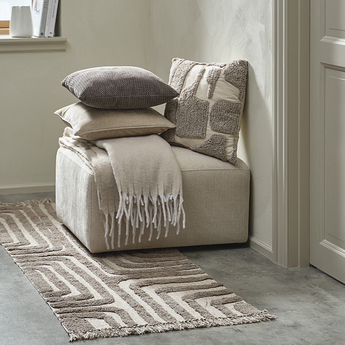 Tapis tufté devant un pouf avec coussins et plaid assortis