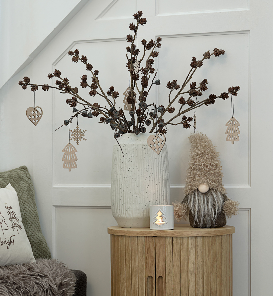 Une petite table avec un vase de décorations de Noël et un lutin de Noël à côté