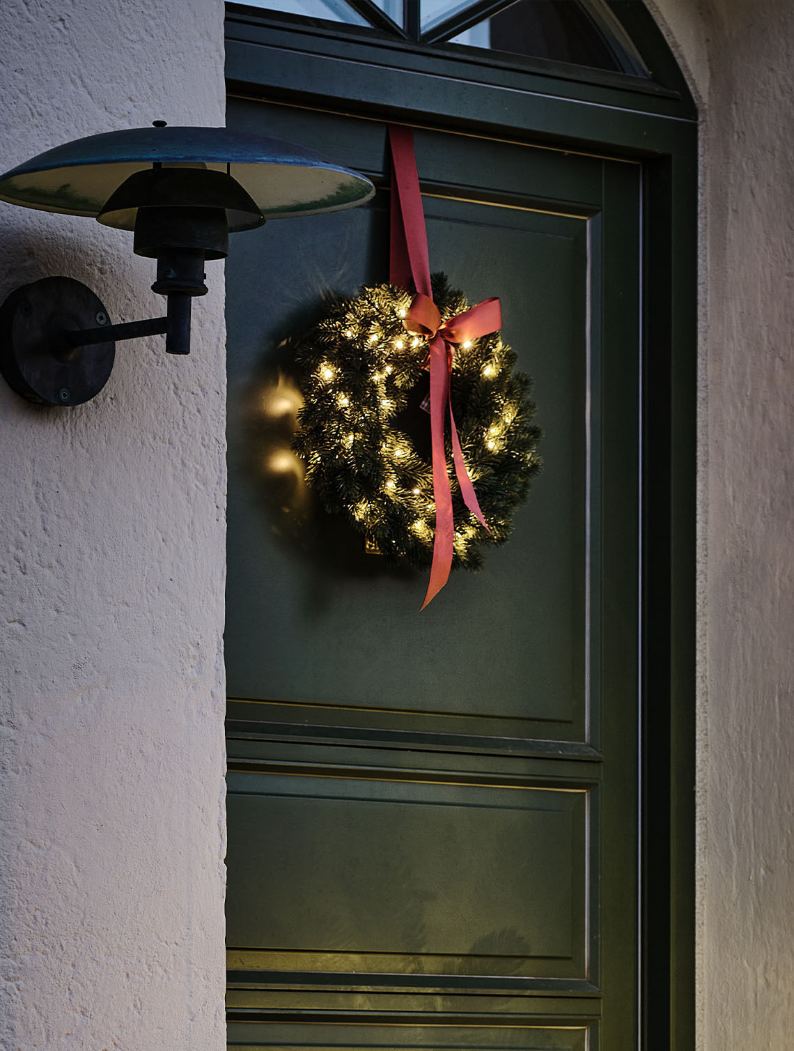 Buitenkerstkrans verlicht met kleine lampjes, op een deur gehangen.
