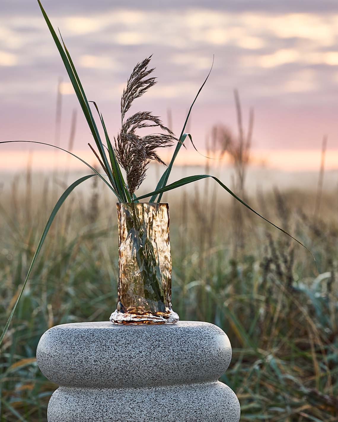 Hoge vaas op pedestal in de duinen bij een strand