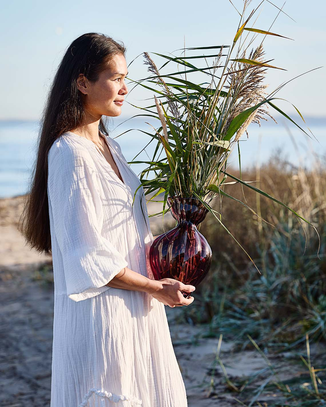 Vrouw met glazen vaas met organische vorm op het strand 