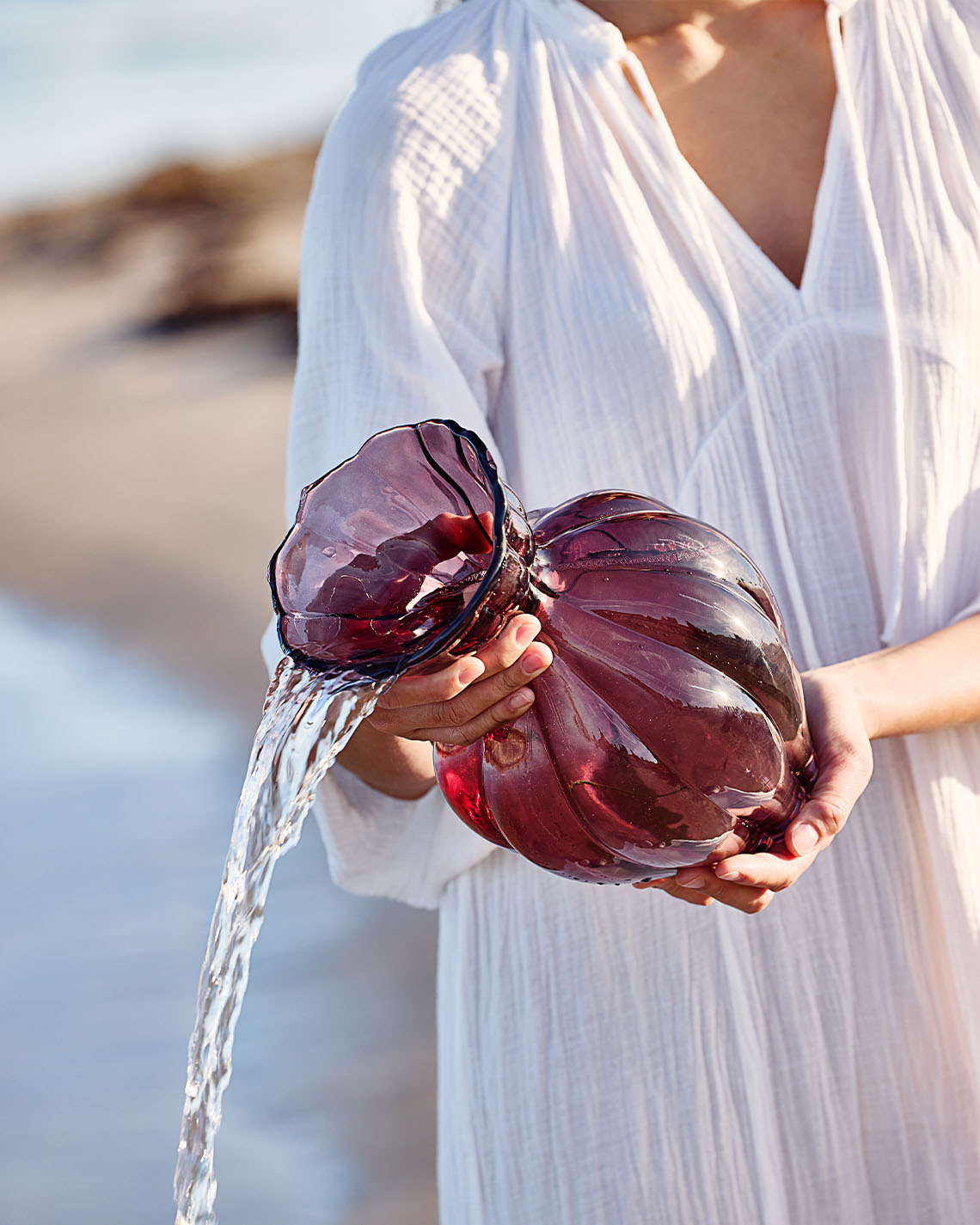 Glazen vaas in auberginekleur, vastgehouden door een vrouw op het strand