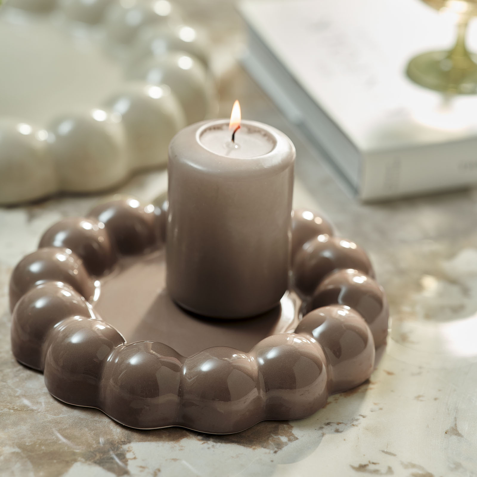 Brandende kaars en licht chocoladebruin decoratief dienblad met bobbels of bubbelachtige randen