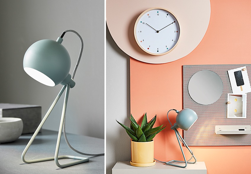 Green table lamp surrounded by wall clock, yellow plant pot and noticeboard with postcards
