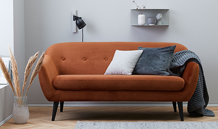 Woonkamer met oranje zitbank gevuld met kussens en een plaid