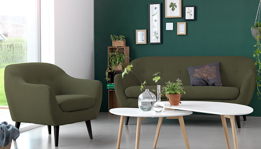 Een woonkamer met een groene velours zitbank en een fauteuil met twee salontafels