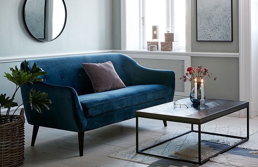 Een woonkamer met een blauwe velours zitbank en een salontafel