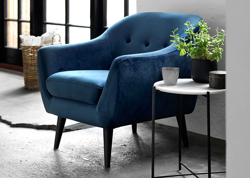 Een woonkamer met een blauw velours fauteuil en een salontafel