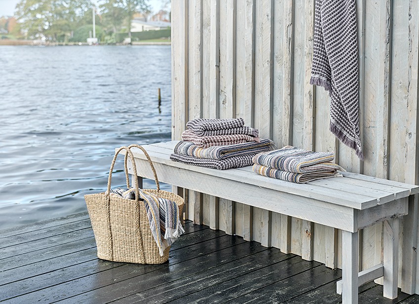 Luxe handdoeken op een bankje en in een rieten tasje bij een meer