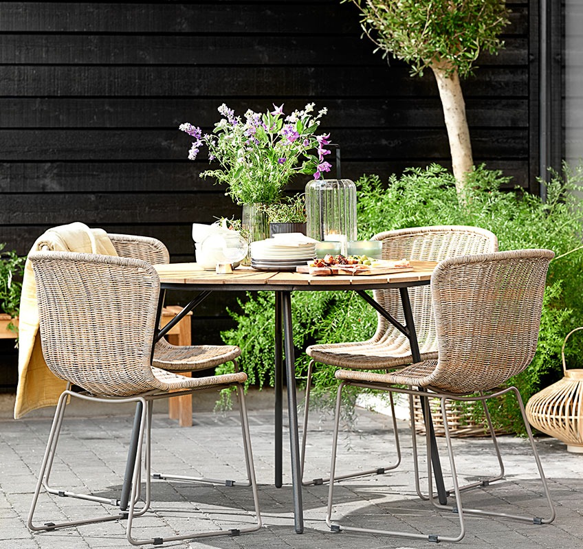 Vier stapelstoelen rond een ronde tuintafel op een patio