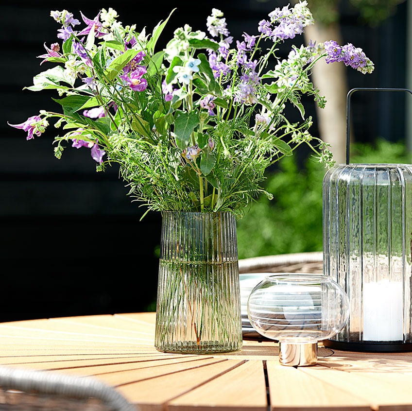 Glazen vaas en lantaarns op een ronde tuintafel 