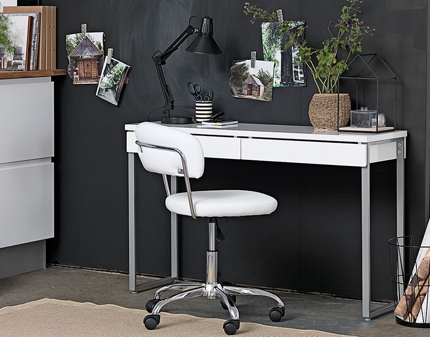 Klein wit bureau met laden en een witte bureaustoel tegen een zwarte muur 