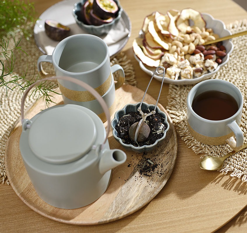 Wooden tray with green teapot and mugs and small bowls with snacks and tea