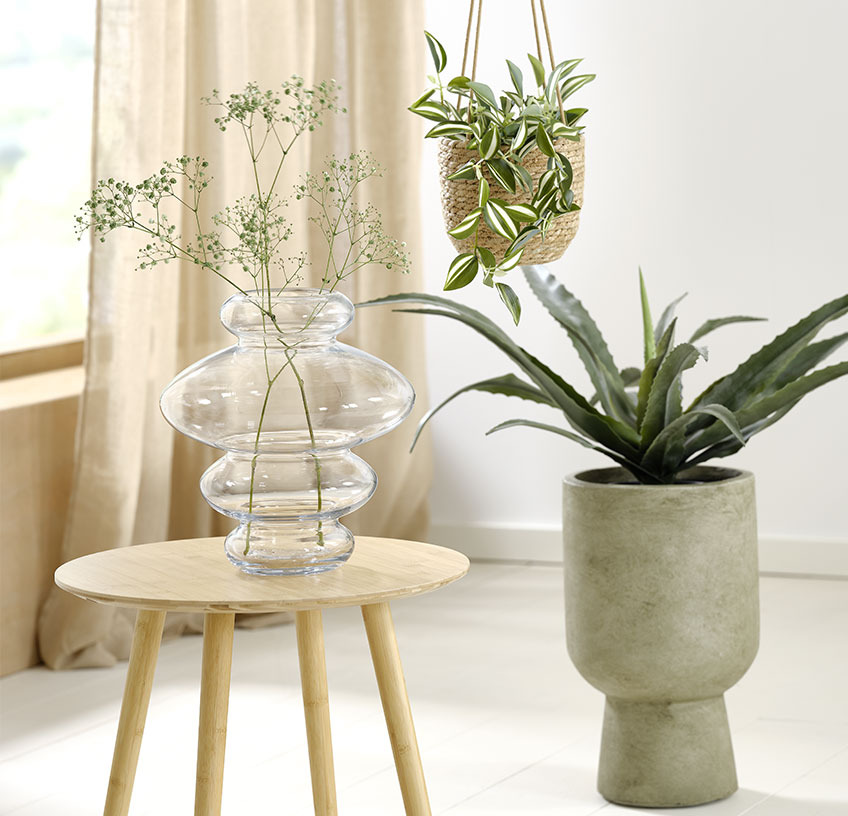 Glazen vaas op een bijzettafel, hangende plantenpot en groene plantenpot met kunstplanten