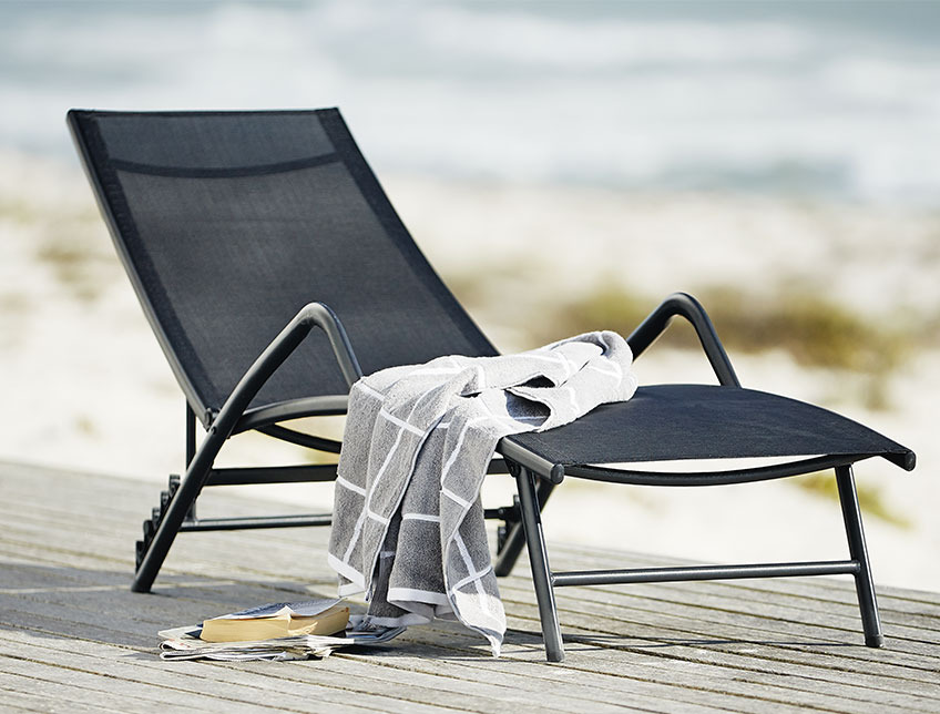 Black sun lounger with armrests on a patio by the beach