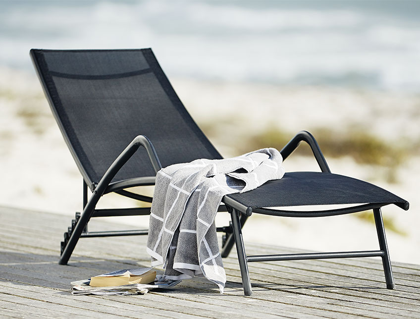 Bain de soleil noir avec accoudoirs sur un patio au bord de la plage