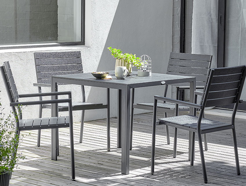 Table de jardin carrée avec quatre chaises empilables sur une terrasse ensoleillée