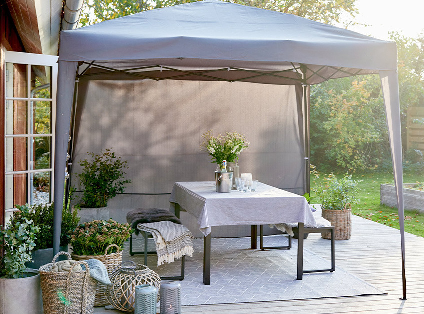 Tonnelle grise avec une table et des bancs décorés, installée sur une terrasse