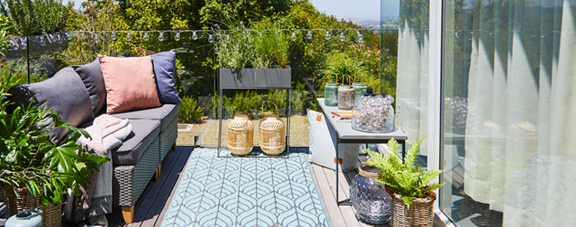 Klein balkon met meubelen, sierkussens en bloempotten